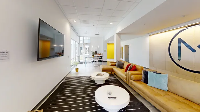 MARQ lounge area featuring a sleek TV, inviting yellow sofas, chic round coffee tables, and natural light from large windows.