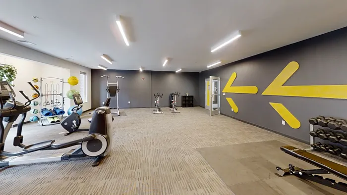 Spacious and well-equipped fitness center the The MARQ  featuring modern exercise machines, vibrant wall decor, and ample floor space for workouts.