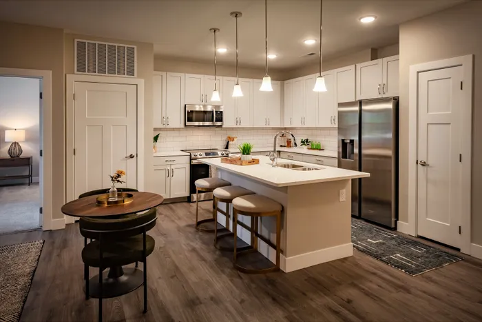 Modern kitchen with sleek white cabinetry, elegant pendant lighting, and a spacious island with seating in a stylish apartment setting.