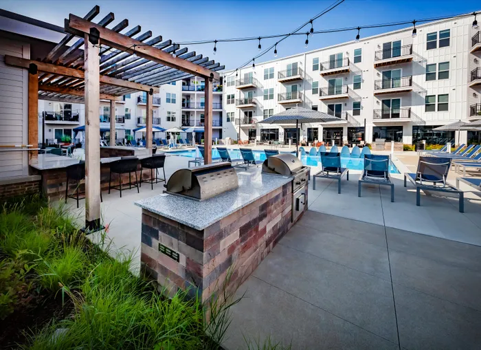 Modern apartment complex featuring stylish outdoor kitchen, grilling stations, and inviting pool area with lounge seating.
