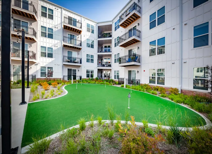 Modern apartment complex with balconies overlooking a pristine putting green surrounded by vibrant landscaping.
