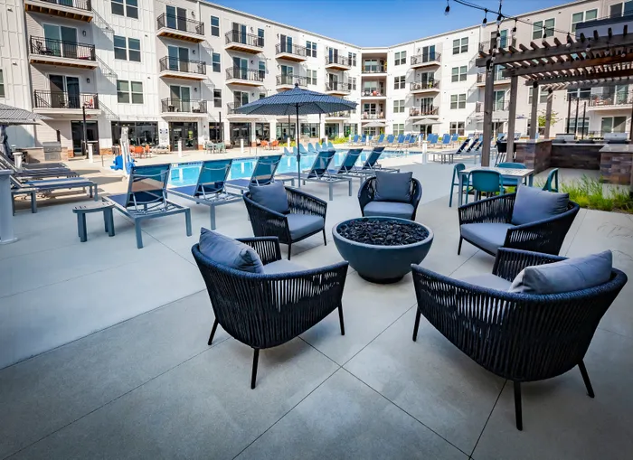 Luxurious apartment complex courtyard featuring a sparkling pool, stylish lounge chairs, cozy fire pit, and modern outdoor seating.