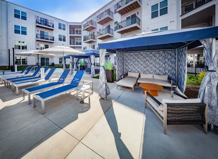 Luxury apartment complex featuring a vibrant outdoor lounge area with stylish cabanas, shaded seating, and modern loungers, perfect for relaxation.