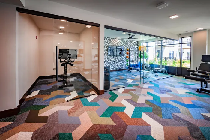 Modern fitness center with vibrant geometric flooring, featuring exercise equipment and a bright, open layout.