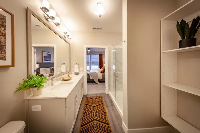 Modern bathroom with elegant fixtures, featuring a large vanity, glass-enclosed shower, and view into a cozy bedroom.