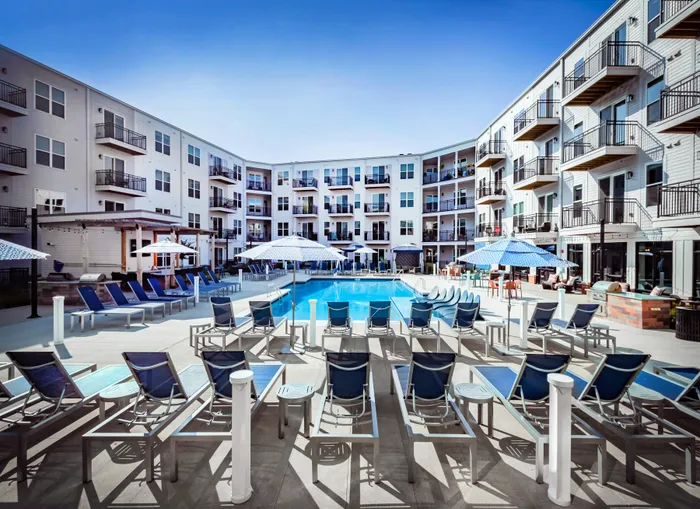 Luxurious apartment complex with a sparkling pool, inviting lounge chairs, and stylish balconies under a clear blue sky.