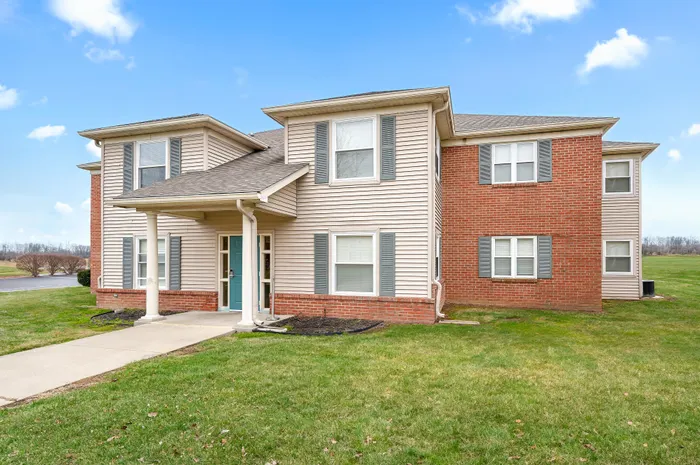 Charming two-story apartment building with a brick and siding exterior, set against a bright blue sky, surrounded by lush green lawns.