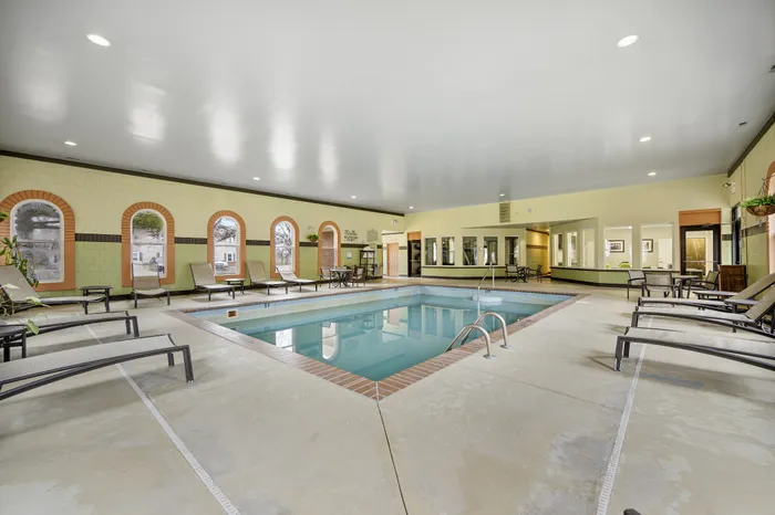 Luxurious indoor swimming pool with stylish lounge chairs and elegant arched windows, offering a serene and relaxing atmosphere.