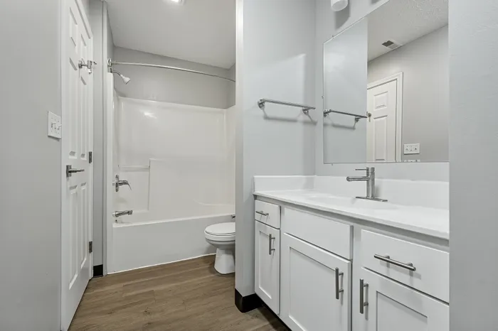 Bright and modern bathroom featuring sleek white cabinetry, a spacious vanity, and elegant wood flooring.