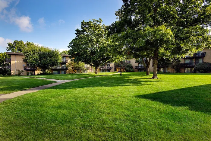 Charming apartment complex surrounded by lush green lawns and mature trees, offering a serene and inviting atmosphere.