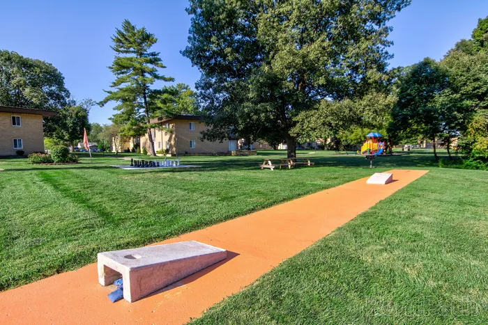 Serene apartment complex with lush green lawns, outdoor seating, a playground, and a giant chess set, ideal for relaxation and family activities.