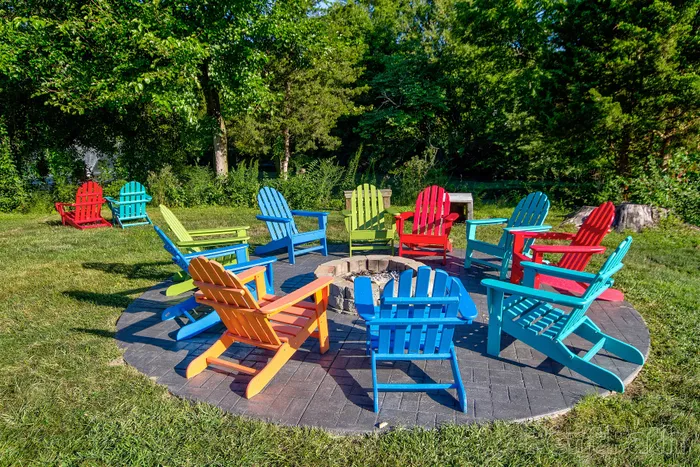 Vibrant outdoor seating area with colorful Adirondack chairs surrounding a cozy fire pit, nestled in lush greenery.