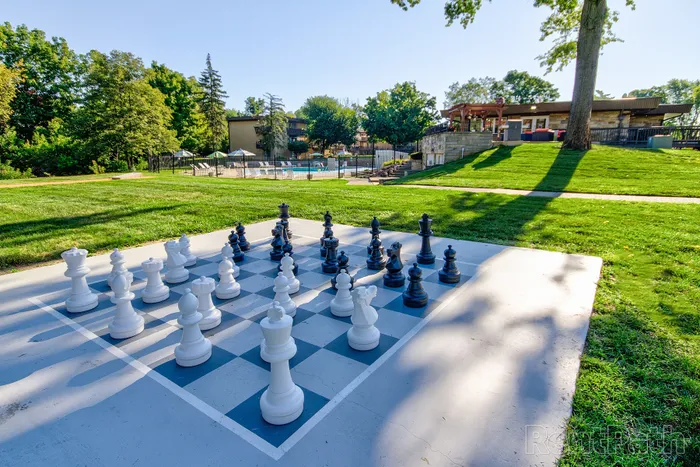 Charming outdoor area with large chess set overlooking a refreshing pool, surrounded by lush greenery and modern amenities.