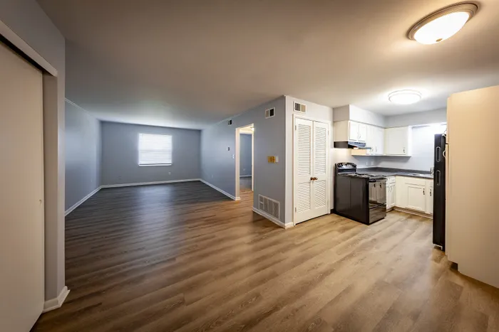 Modern apartment interior showcasing an open-concept living area with sleek hardwood floors and a cozy kitchen with white cabinetry.