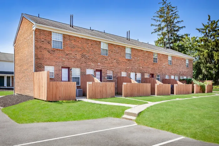 Charming brick exterior with private fenced patios and lush green surroundings, offering a welcoming community vibe.