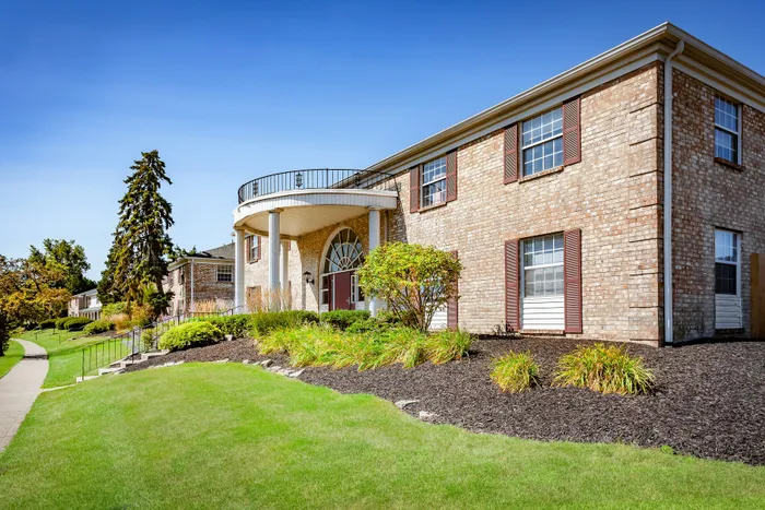 Charming brick apartment building with classic architecture, surrounded by lush greenery and a serene walkway.
