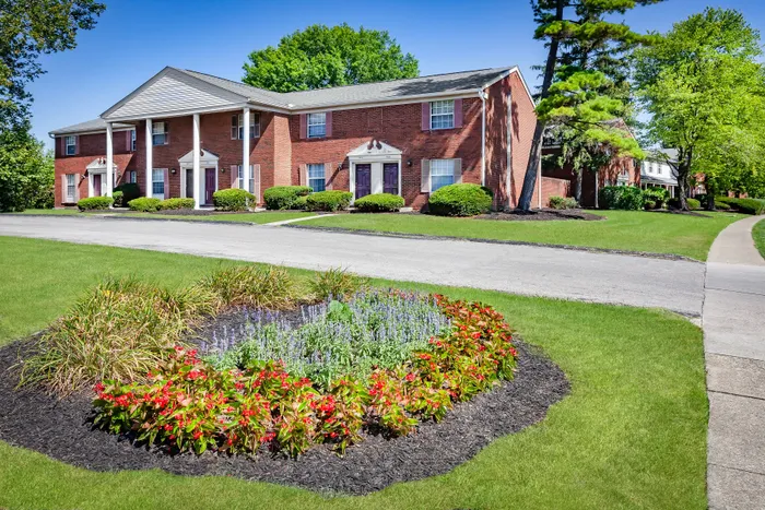 Charming brick apartment complex highlighted by colorful flower beds, lush green lawns, and classic architectural details.