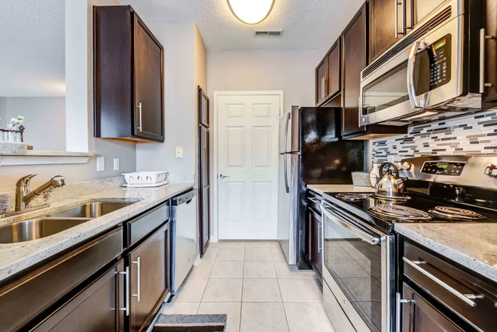 Elegant kitchen with dark wood cabinetry, modern stainless steel appliances, and stylish tile backsplash.