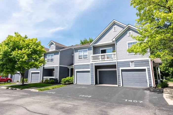 Charming suburban apartment building with modern gray siding, balconies, and attached garages, surrounded by lush greenery and vibrant trees.