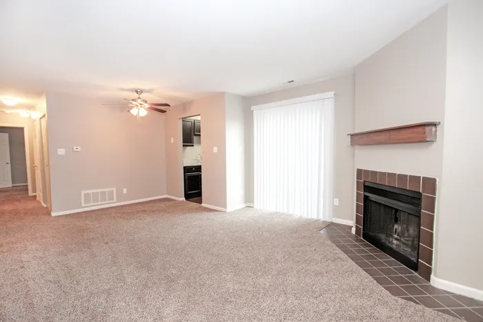 Inviting living room featuring plush carpeting,  fireplace, and a ceiling fan, with bright sliding doors leading to the kitchen.