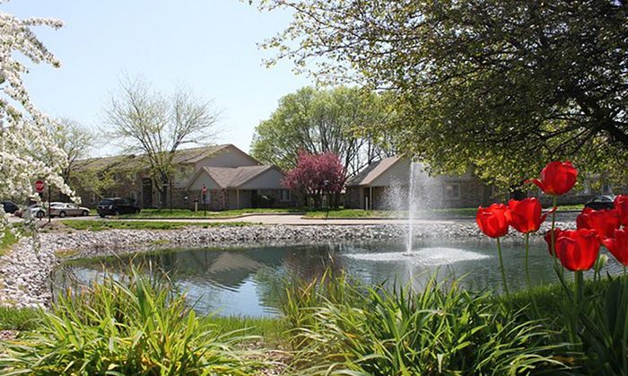 Serene apartment community with a charming pond and a refreshing fountain surrounded by lush greenery.