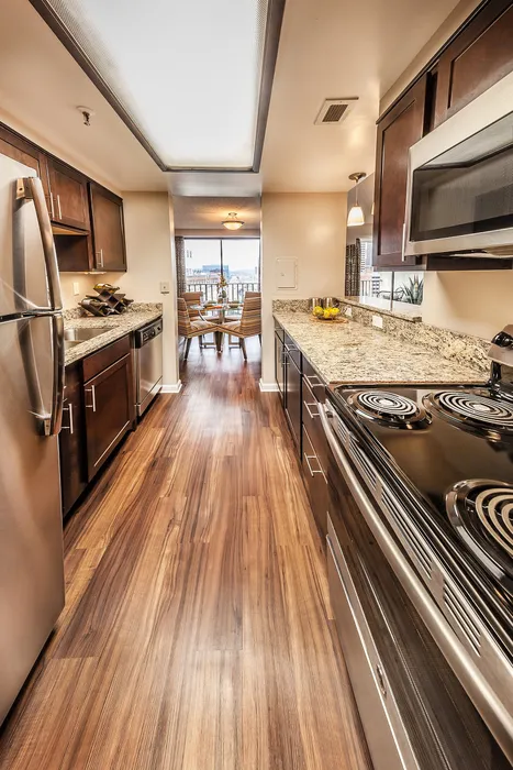 Modern kitchen with sleek stainless steel appliances, rich wood cabinetry, and elegant granite countertops, opening to a bright dining area with city views.