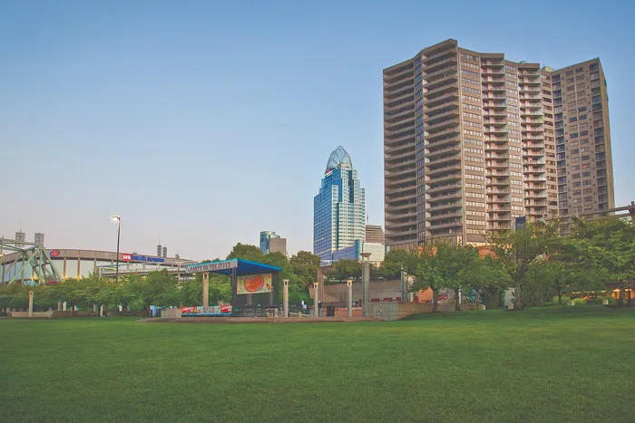 Vibrant cityscape featuring modern high-rise apartments, lush green park, and skyline under a clear blue sky.