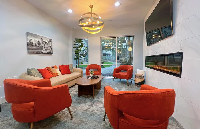 Inviting clubhouse lounge with modern decor, featuring vibrant orange chairs, a cozy beige sofa, and a sleek fireplace.