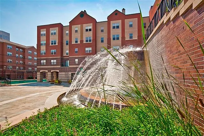 Vibrant apartment community with a refreshing fountain, surrounded by lush greenery and modern architecture.