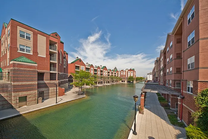Charming waterfront apartment buildings with modern architecture, overlooking a serene canal and vibrant blue sky.