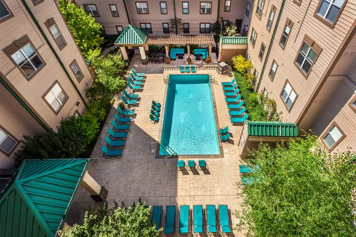 Elegant apartment courtyard with a sparkling pool, surrounded by lush greenery and stylish sun loungers, perfect for relaxation.