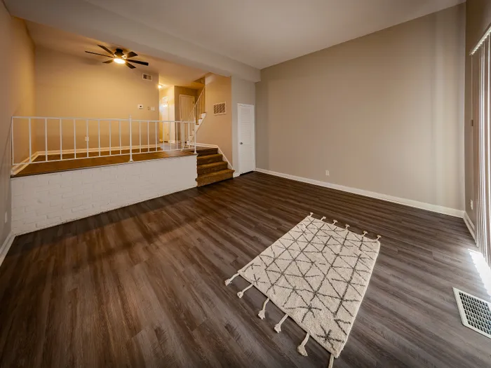 Elegant living space with warm wooden flooring, plush area rug, and a cozy elevated landing area beneath soft lighting.