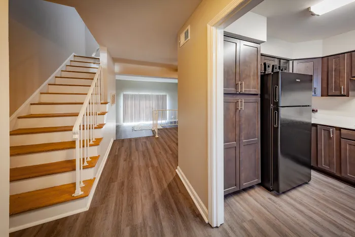 Modern apartment interior featuring sleek wooden staircase, spacious kitchen with dark cabinetry, and bright open living area.