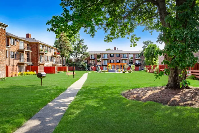 Vibrant apartment complex featuring lush green lawns, inviting outdoor seating area, and charming red brick buildings under a clear blue sky.