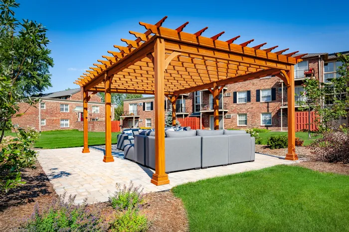 Charming outdoor patio with modern pergola featuring comfortable seating, nestled in a lush green apartment courtyard.