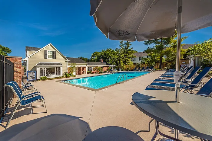 Brockton Apartments outdoor pool area with sun loungers and umbrellas, surrounded by lush greenery and modern apartments.