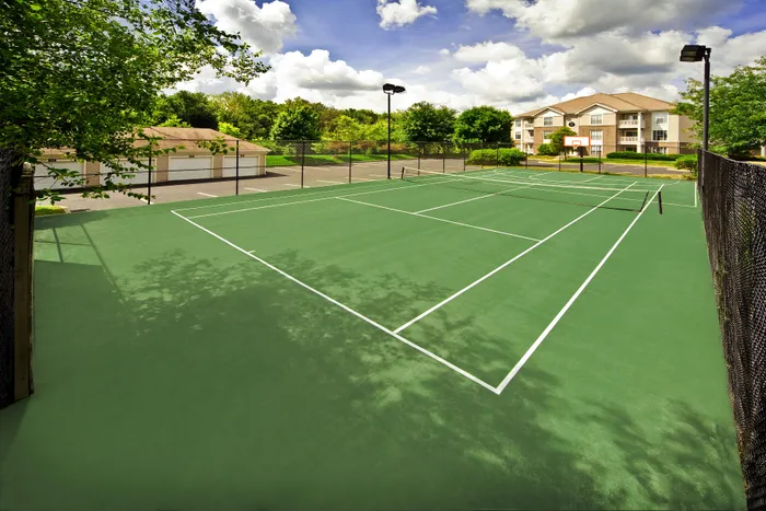 Beautiful outdoor tennis court with lush surroundings near modern apartment complex, perfect for active living.