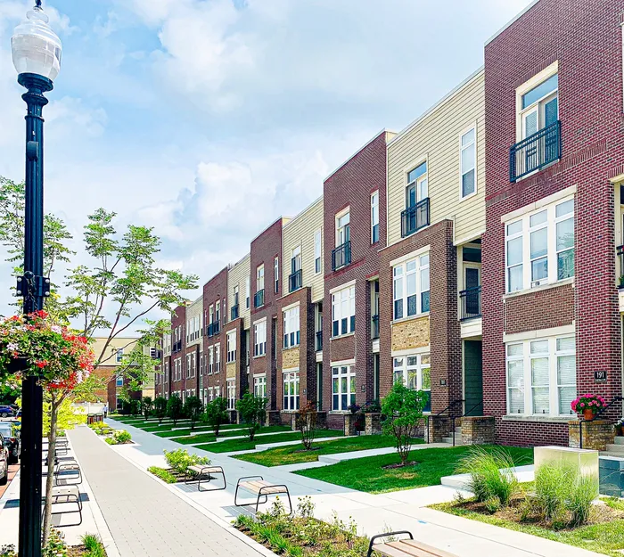 Charming row of modern townhouses with brick facades and large windows, featuring manicured gardens and a tree-lined sidewalk.