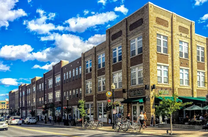 Charming urban apartment building with vibrant street view, featuring stylish brick facade and bustling sidewalks against a bright blue sky.
