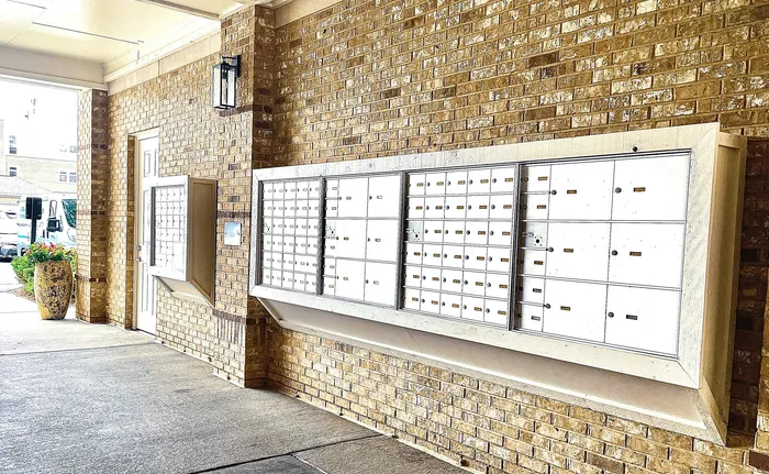 Elegant apartment mailroom with a brick wall backdrop, featuring modern mailboxes and decorative planters.
