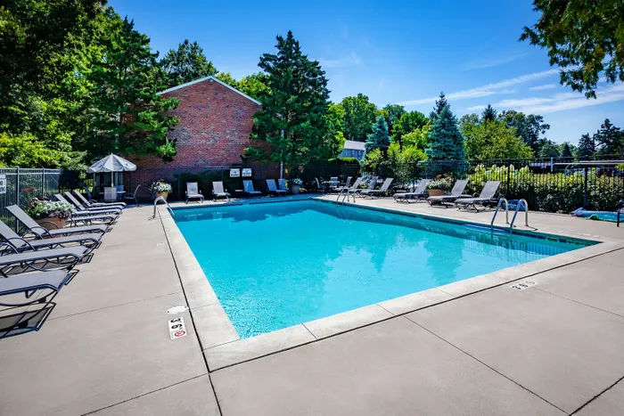 Inviting outdoor pool area with comfortable lounge chairs, surrounded by lush greenery and clear blue skies, perfect for relaxation and sunbathing.