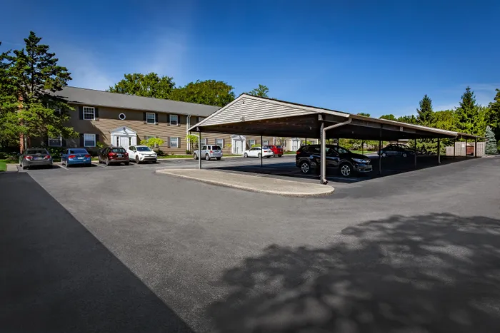 Charming apartment complex with ample covered parking, surrounded by lush greenery and vibrant vehicles, under a clear blue sky.