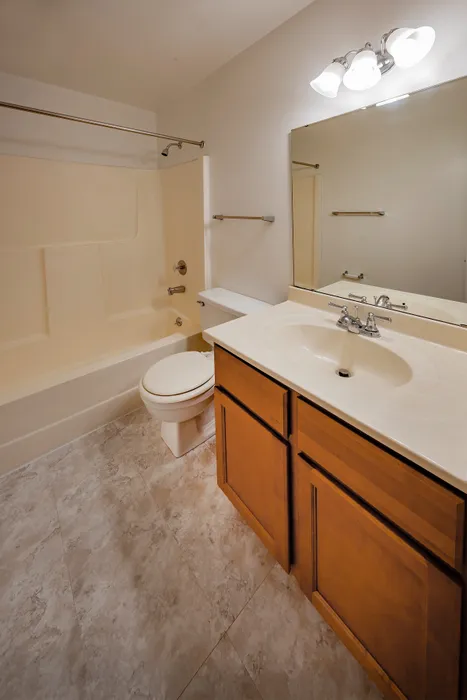 Bright and modern bathroom featuring elegant lighting, a large mirror, and a pristine bathtub with clean tile flooring.