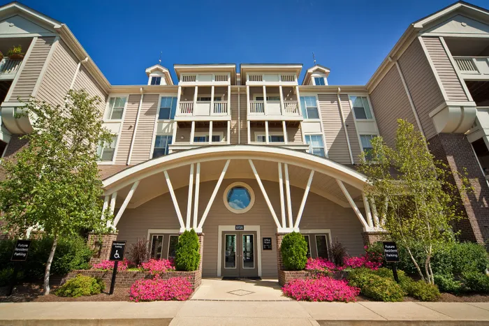 Elegant apartment building entrance with modern architecture, lush greenery, and vibrant flowers, offering inviting charm and curb appeal.