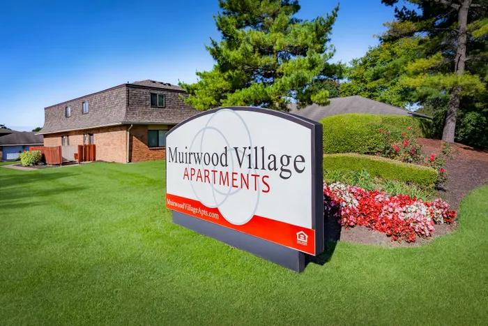 Inviting entrance to Muirwood Village Apartments, showcasing vibrant landscaping and a welcoming sign under a clear blue sky.