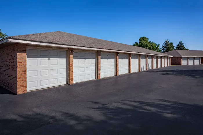 Spacious row of pristine white garage doors with brick accents under a clear blue sky, offering ample parking and storage in a secure and clean environment.