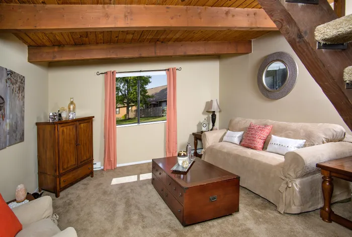 Cozy living room with rustic wooden beams, elegant beige sofa, and a charming wooden coffee table, bathed in natural sunlight from the window.