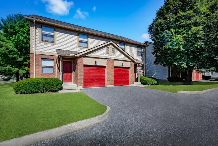 Charming two-story townhouse with vibrant red doors, lush green lawn, and a spacious two-car garage, nestled in a peaceful neighborhood.