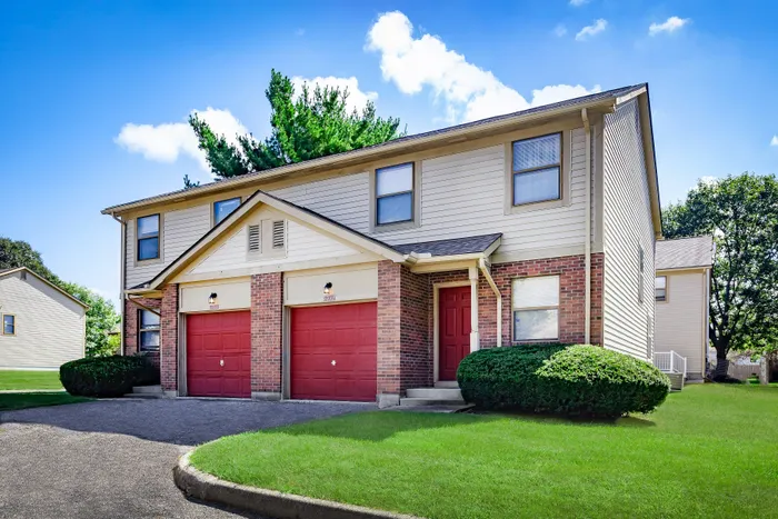 Charming duplex with vibrant red doors, classic brick facade, and lush green lawn under a clear blue sky.