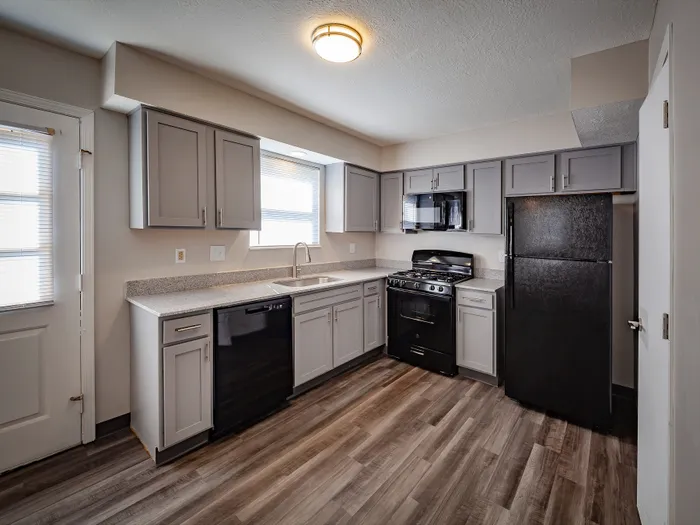 Modern kitchen with sleek gray cabinets, black appliances, and elegant wood flooring, offering a stylish cooking space.